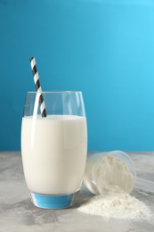 Photo of Delicious protein shake in glass and scoop with powder on gray textured table against light blue background