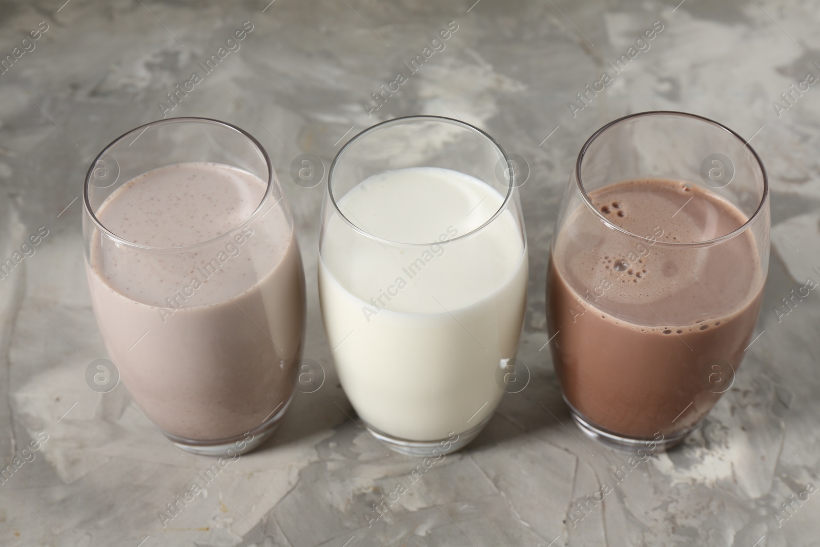 Photo of Delicious protein shakes in glasses on gray textured table, closeup