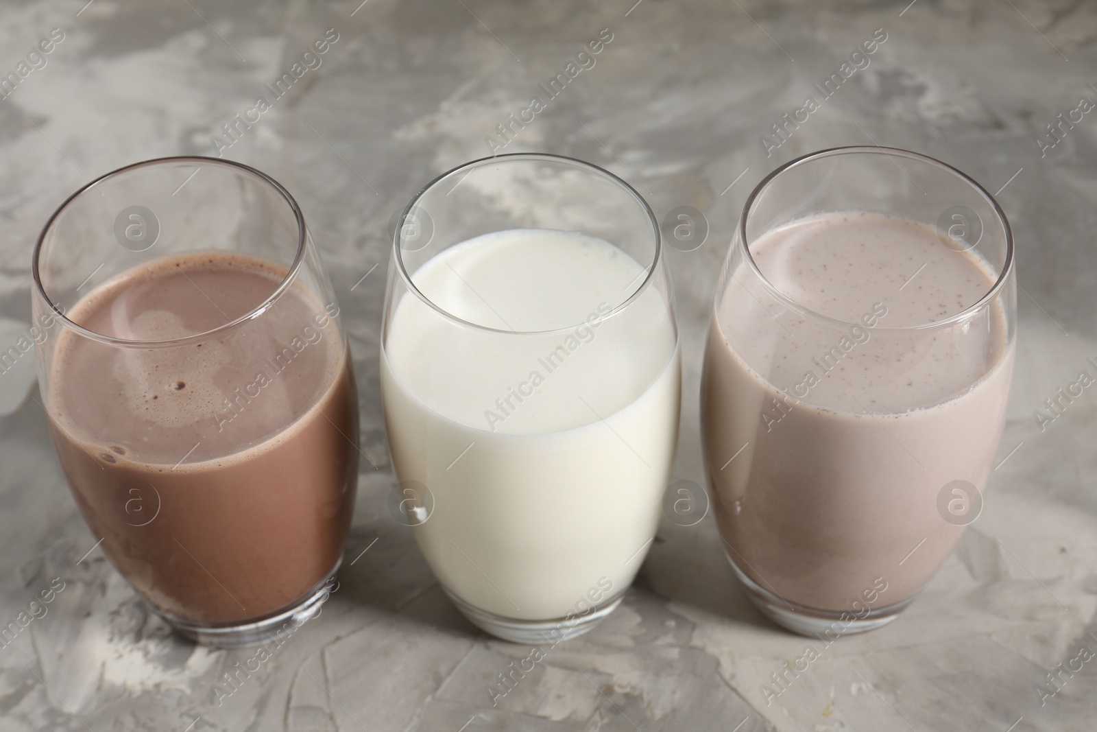 Photo of Delicious protein shakes in glasses on gray textured table, closeup