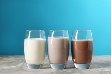 Photo of Delicious protein shakes in glasses on gray textured table against light blue background