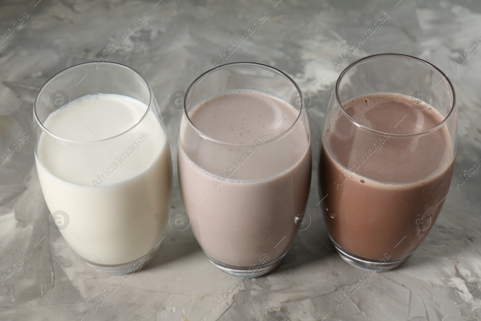 Photo of Delicious protein shakes in glasses on gray textured table, closeup