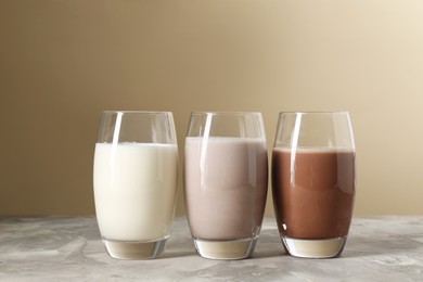 Photo of Delicious protein shakes in glasses on gray textured table against beige background