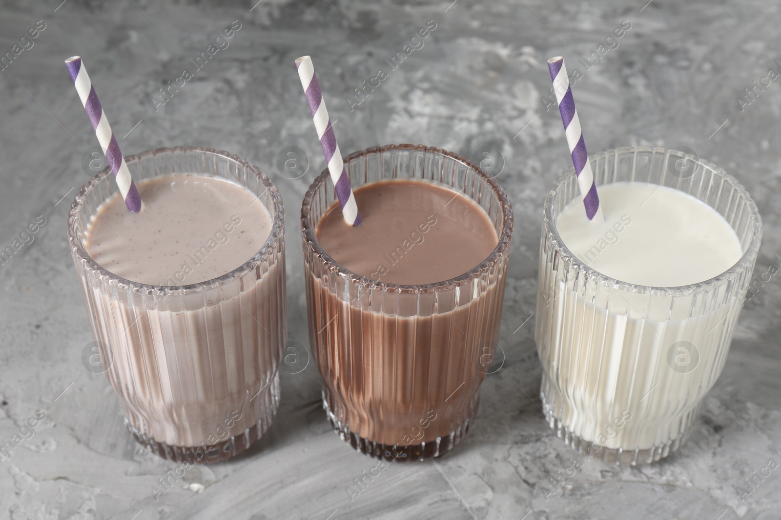 Photo of Delicious protein shakes in glasses on gray textured table, closeup