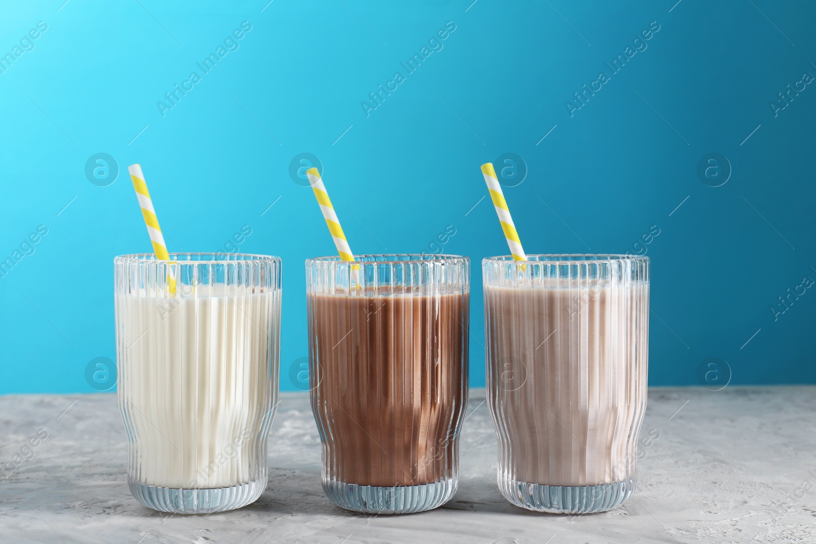 Photo of Delicious protein shakes in glasses on gray textured table against light blue background