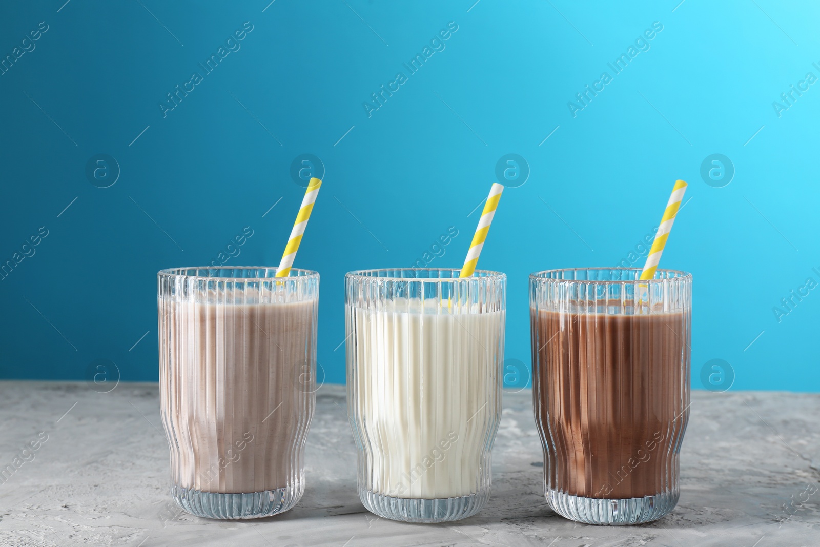 Photo of Delicious protein shakes in glasses on gray textured table against light blue background