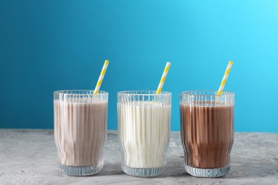 Photo of Delicious protein shakes in glasses on gray textured table against light blue background