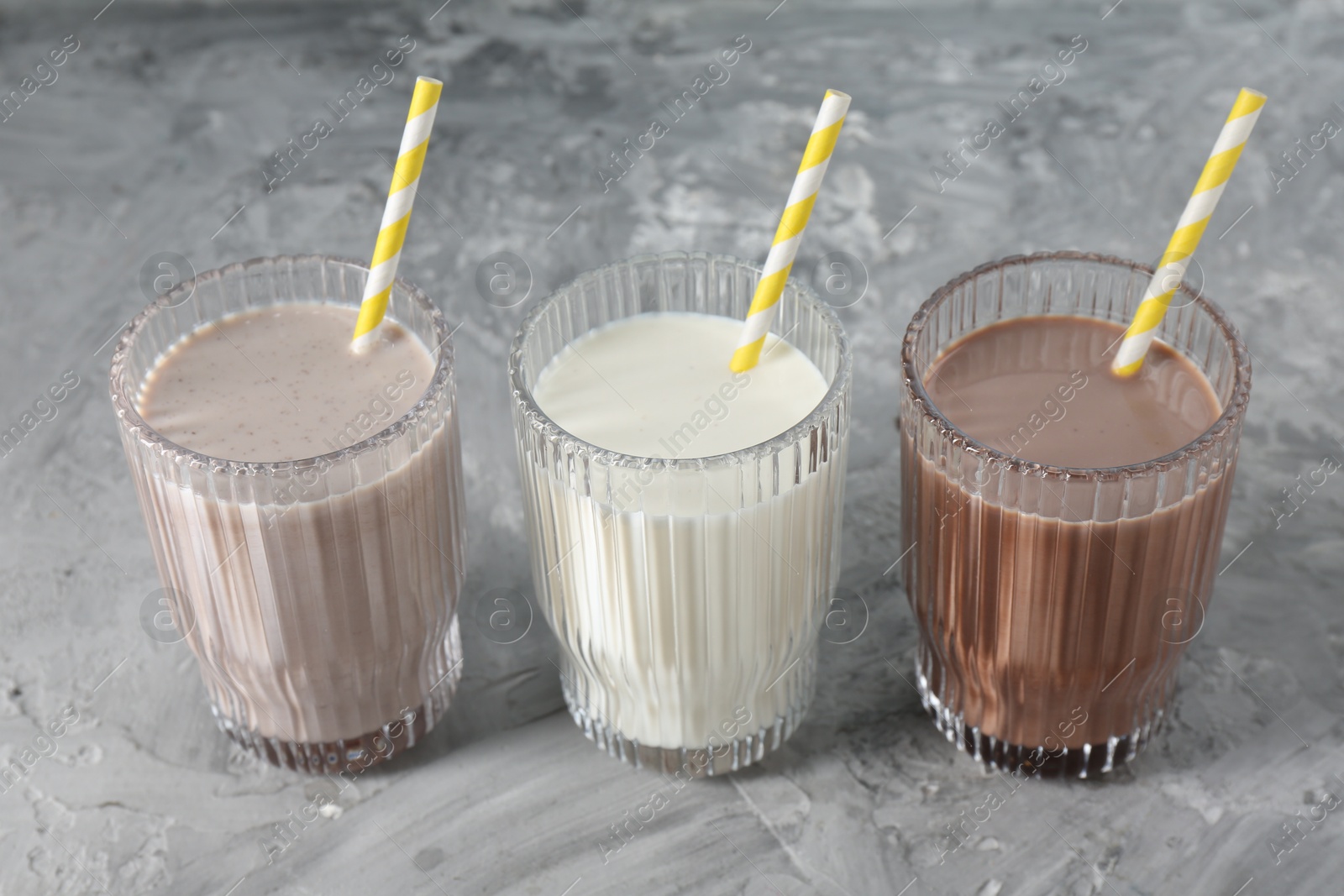 Photo of Delicious protein shakes in glasses on gray textured table, closeup