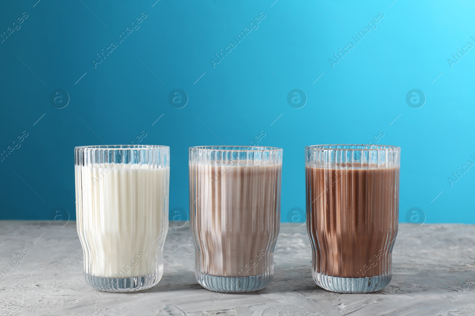 Photo of Delicious protein shakes in glasses on gray textured table against light blue background