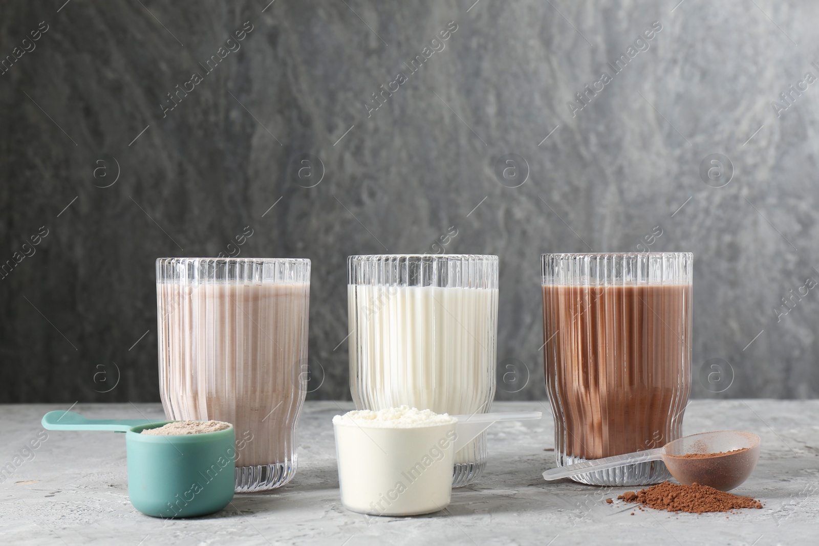 Photo of Delicious protein shakes in glasses and scoops with powder on gray textured table