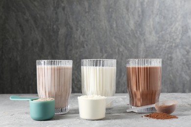 Photo of Delicious protein shakes in glasses and scoops with powder on gray textured table