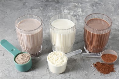 Photo of Delicious protein shakes in glasses and scoops with powder on gray textured table, closeup