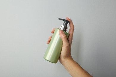 Photo of Woman with shampoo bottle on grey background, closeup