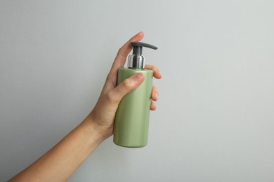 Photo of Woman with shampoo bottle on grey background, closeup