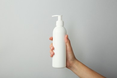 Photo of Woman with shampoo bottle on grey background, closeup