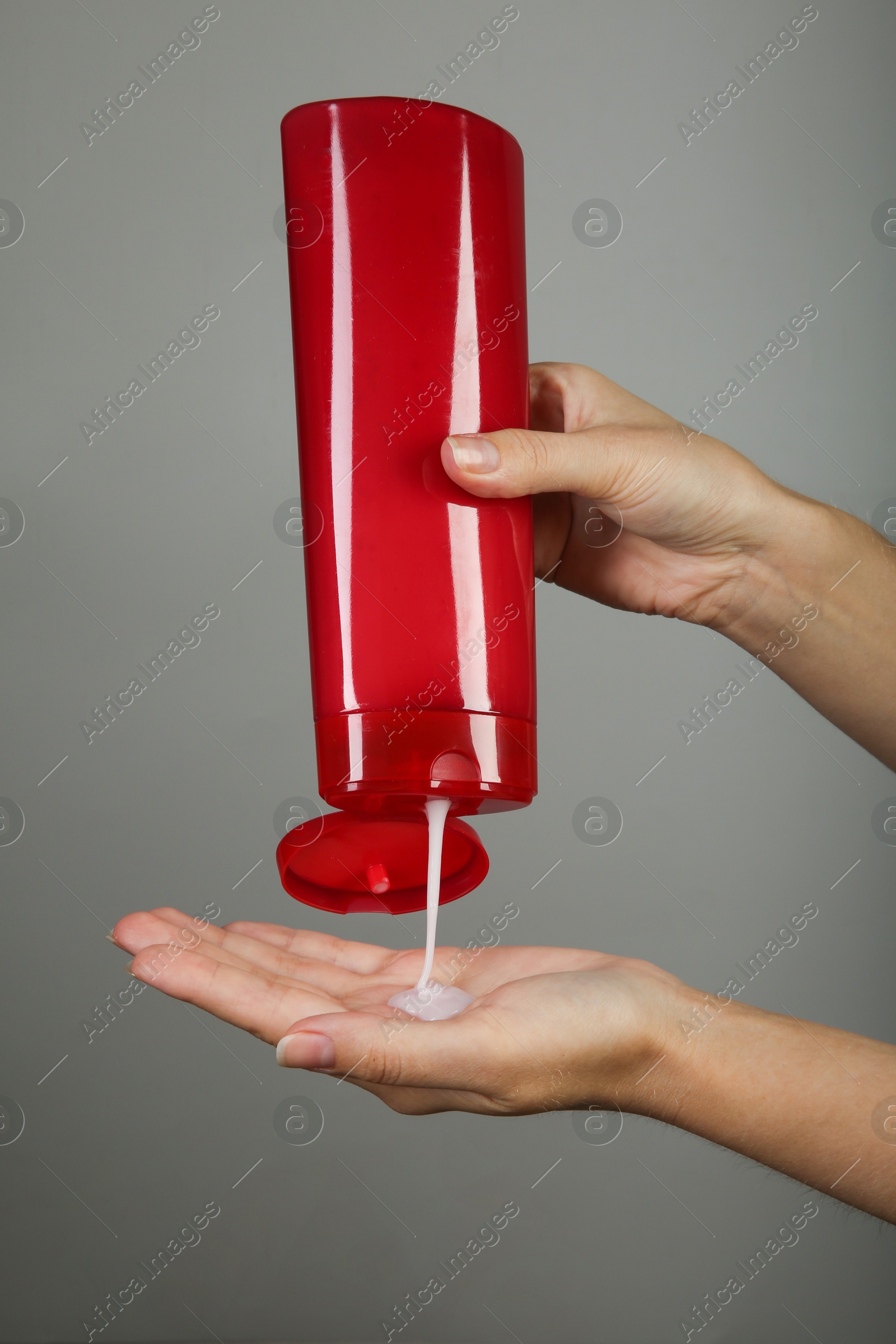 Photo of Woman pouring shampoo onto hand on grey background, closeup