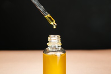 Photo of Dripping tincture from pipette into bottle against color background, closeup