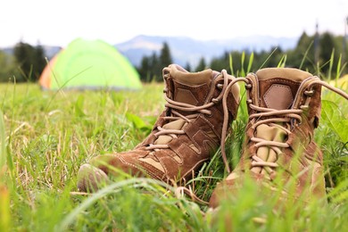 Trekking shoes and camping tent on green grass outdoors, closeup