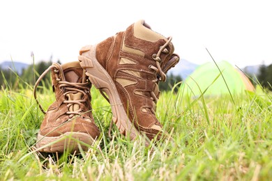 Trekking shoes and camping tent on green grass outdoors, space for text