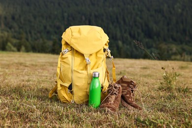 Backpack, thermos and trekking shoes on grass outdoors