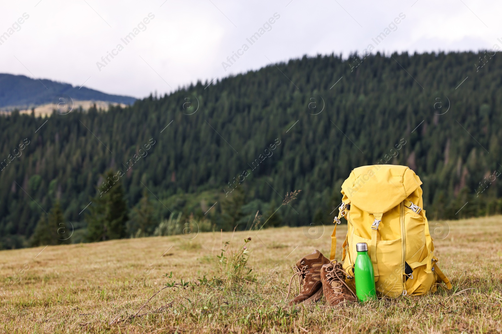 Photo of Backpack, thermos and trekking shoes on grass outdoors, space for text