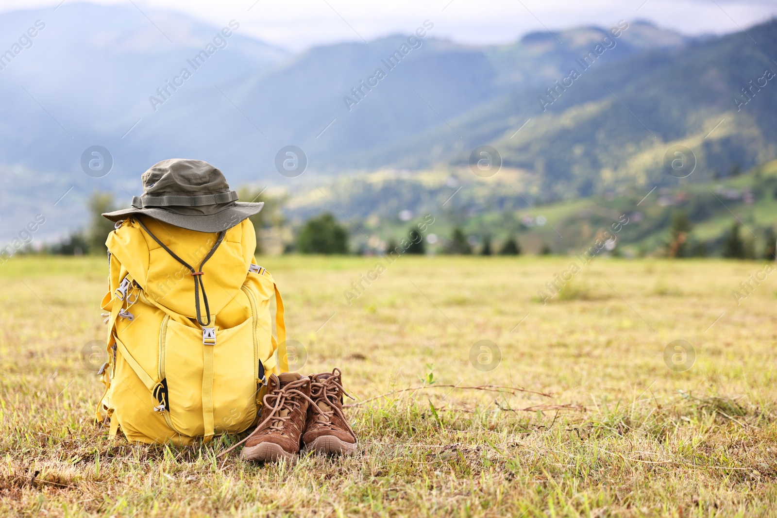 Photo of Backpack, hat and trekking shoes on grass outdoors, space for text