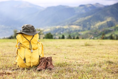 Photo of Backpack, hat and trekking shoes on grass outdoors, space for text