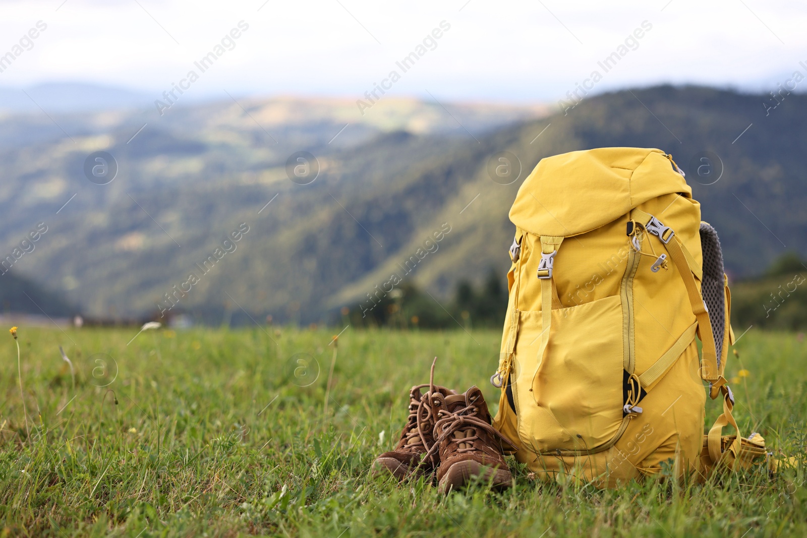 Photo of Backpack and trekking shoes on green grass outdoors, space for text