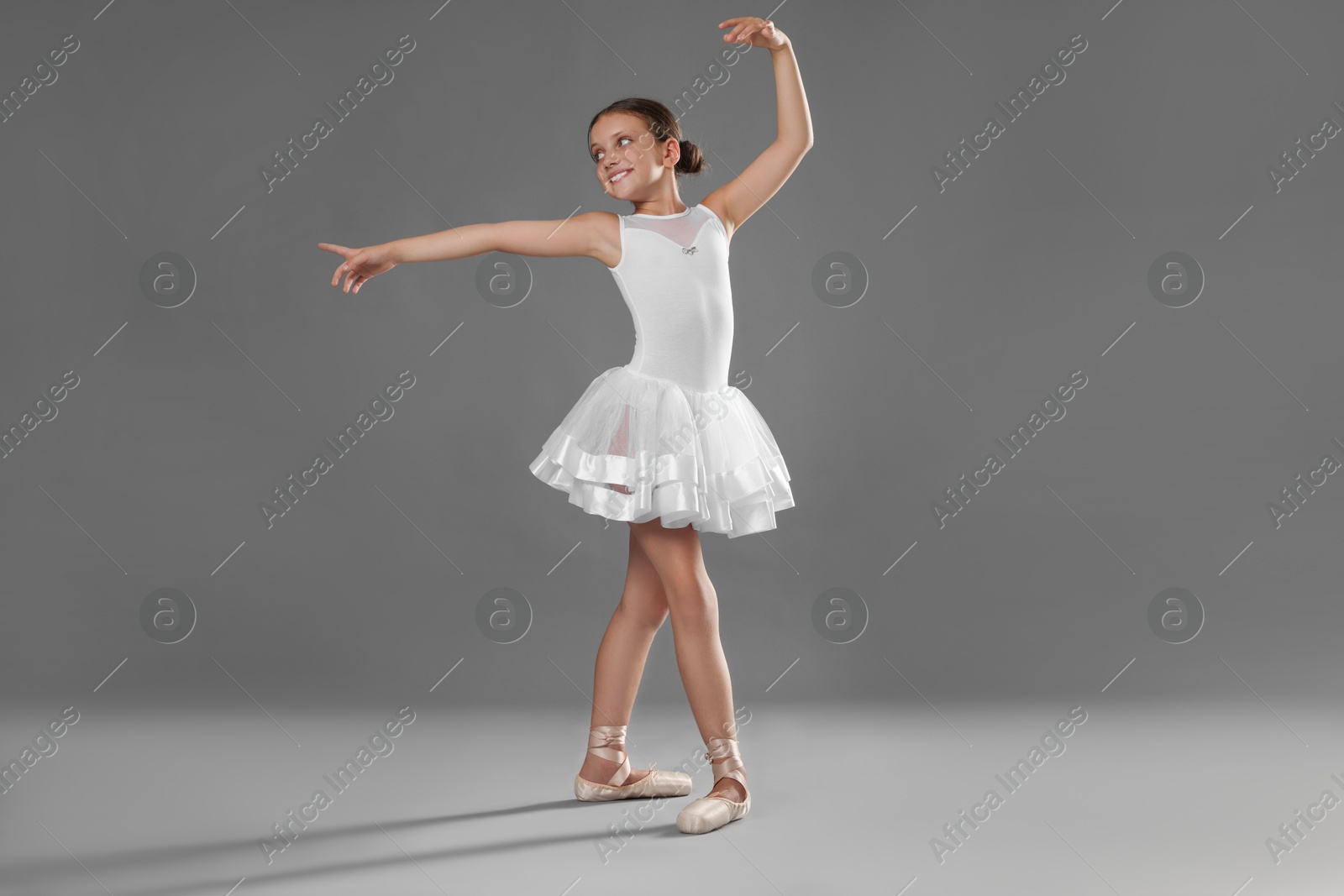 Photo of Cute little ballerina dancing on grey background