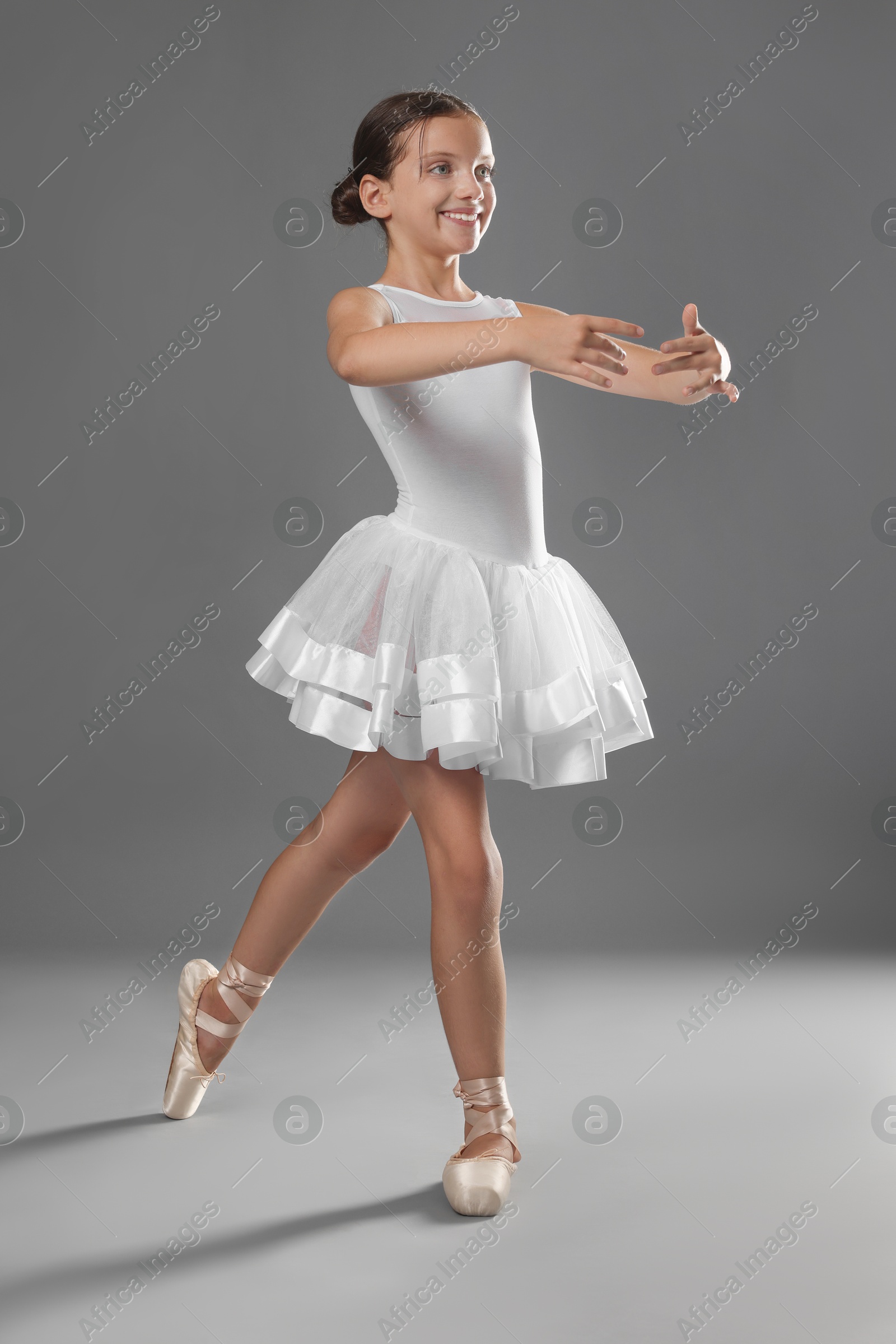 Photo of Cute little ballerina dancing on grey background