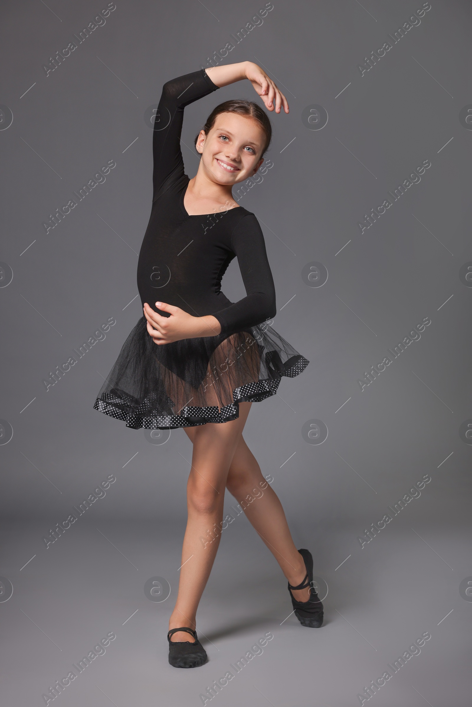 Photo of Little ballerina practicing dance moves on grey background