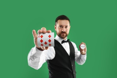 Croupier holding card and dealer button on green background, selective focus