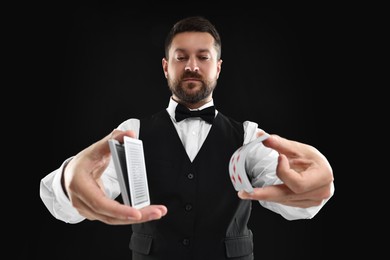 Professional croupier shuffling cards on black background