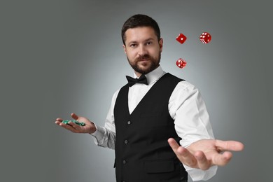 Professional croupier with dice and casino chips on grey background