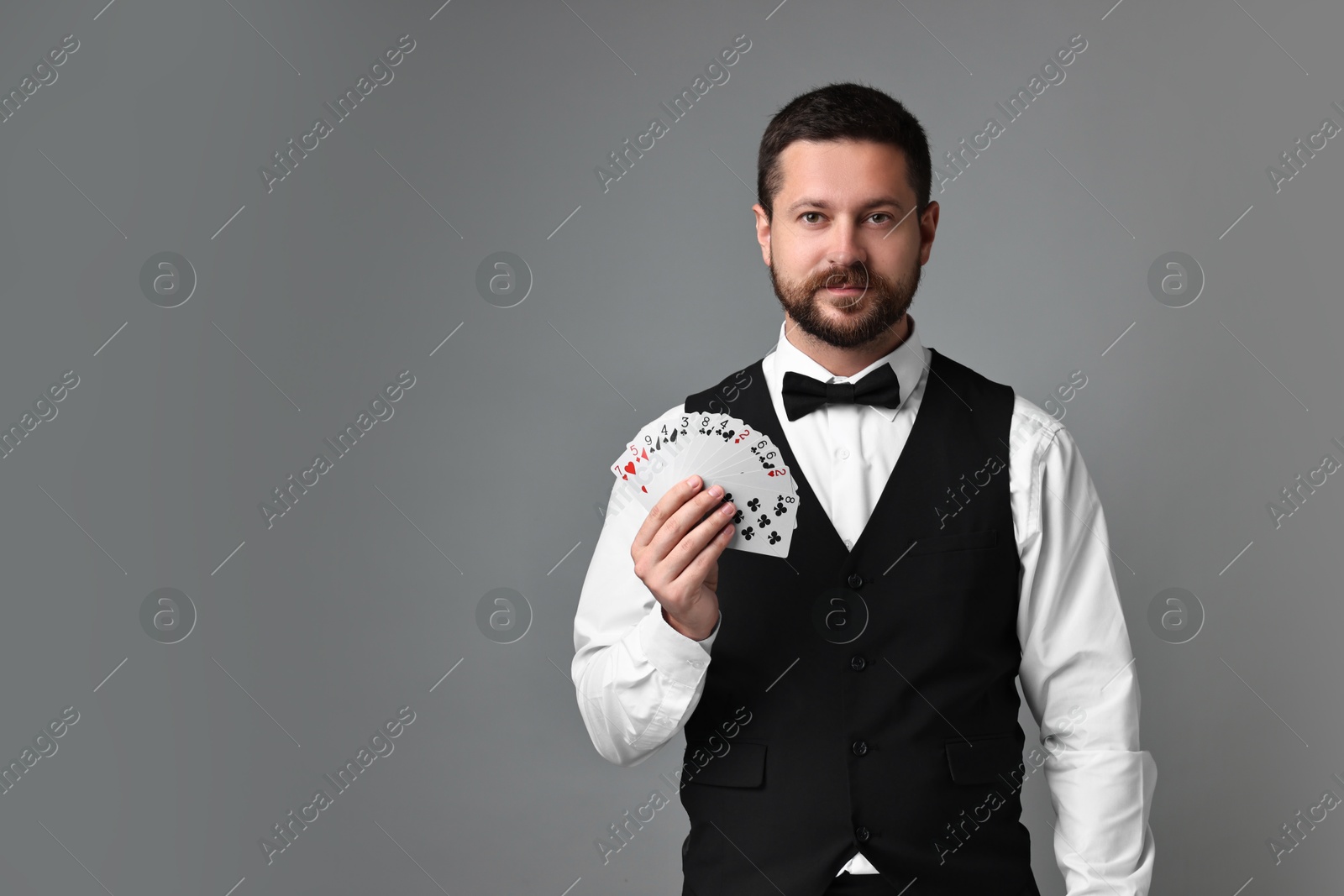 Photo of Professional croupier with playing cards on grey background, space for text