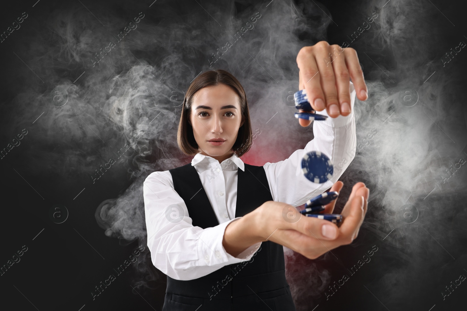 Photo of Croupier holding casino chips on dark red background with smoke