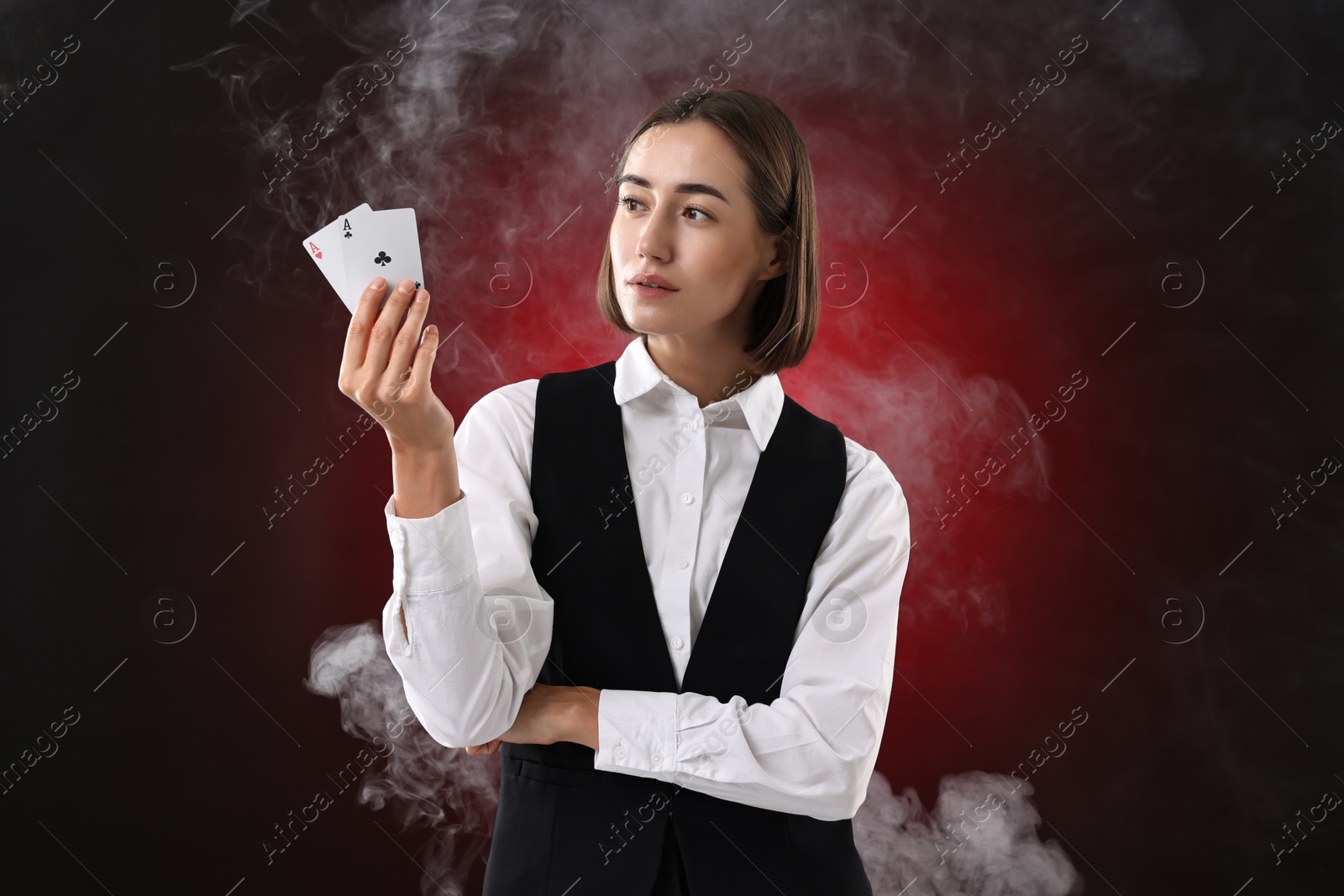 Photo of Croupier holding playing cards on dark red background with smoke