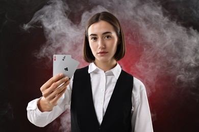 Croupier holding playing cards on dark red background with smoke