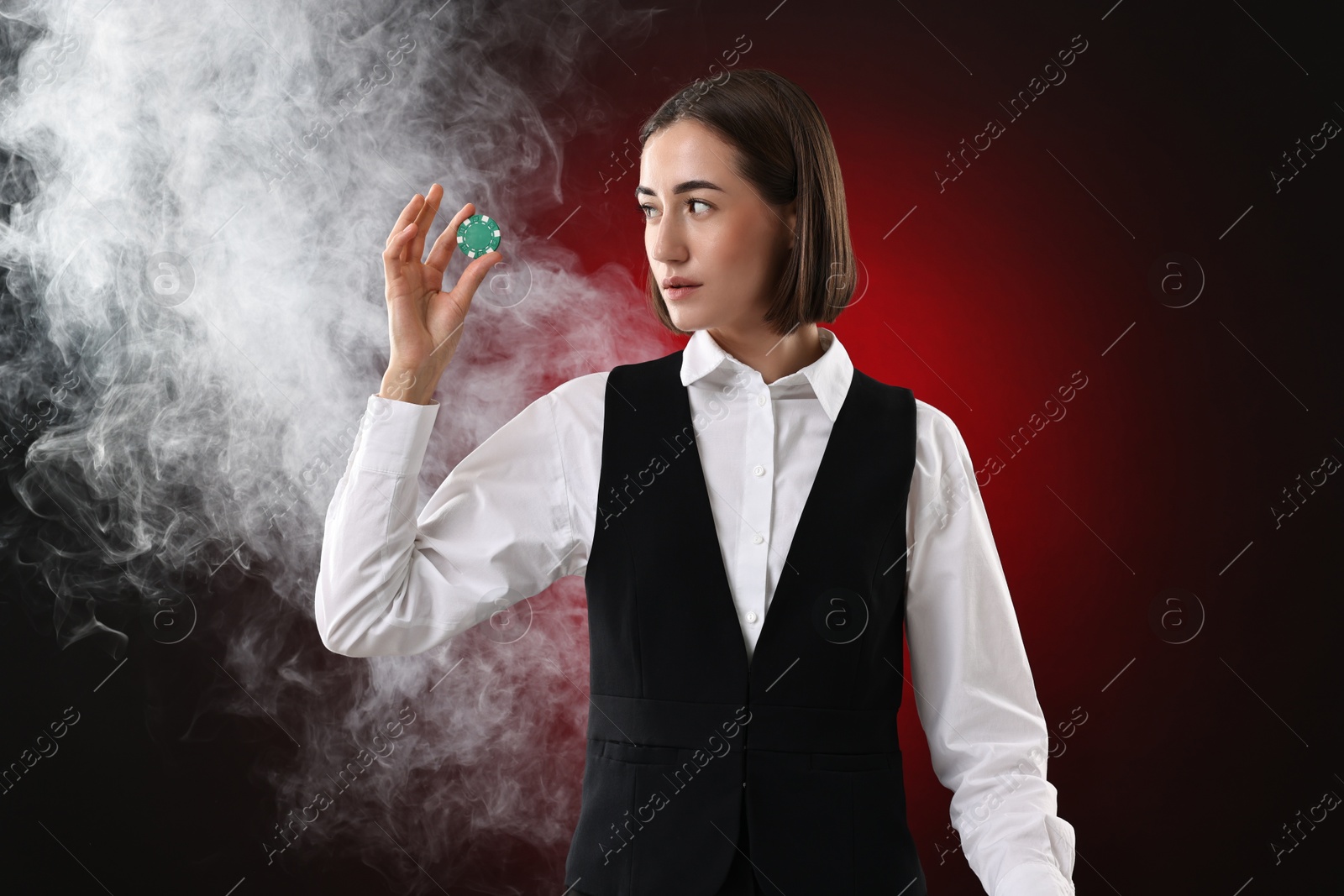 Photo of Croupier holding casino chip on dark red background with smoke