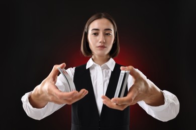 Professional croupier shuffling cards on dark red background