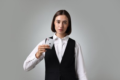 Professional croupier with playing cards on grey background