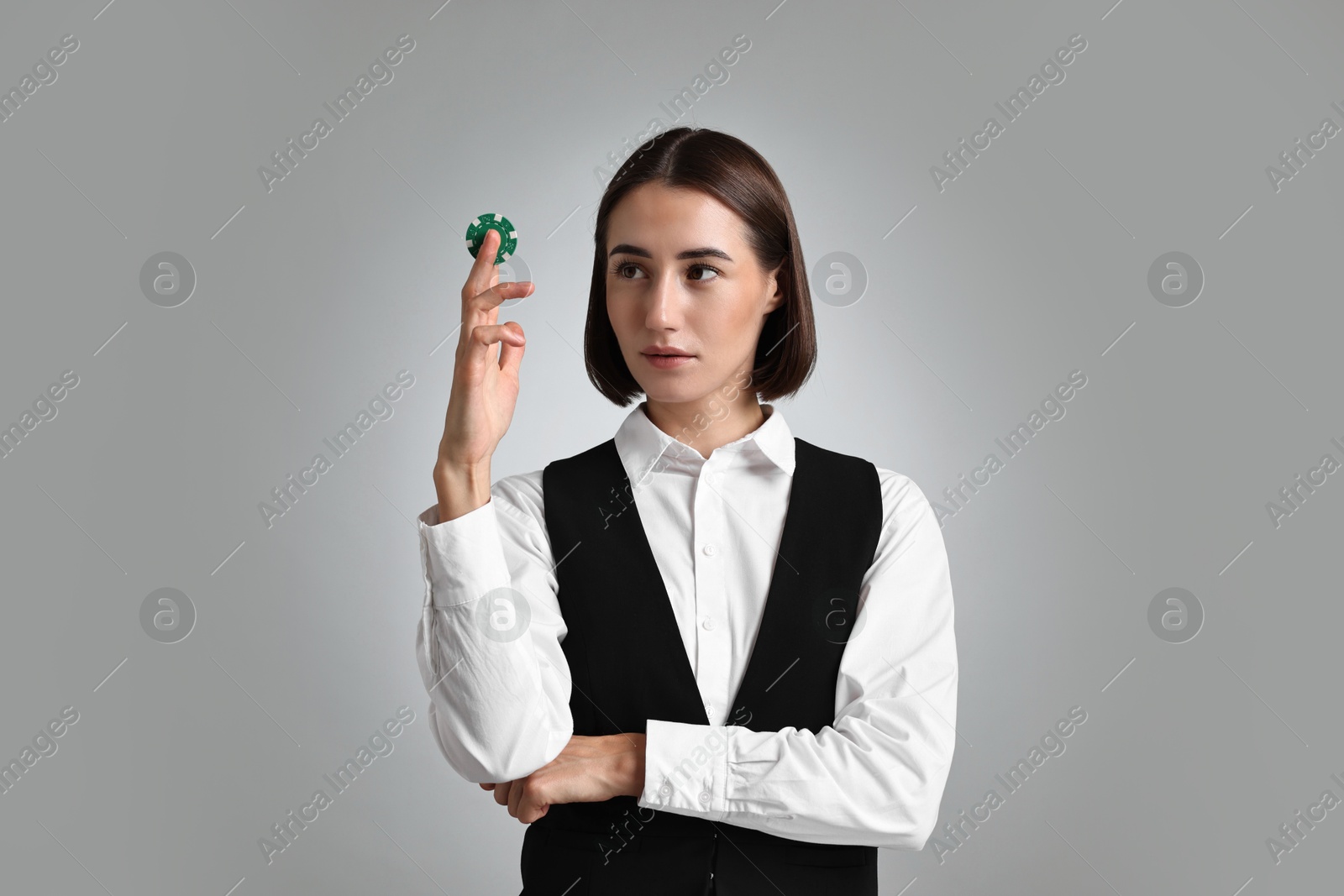 Photo of Professional croupier with casino chip on grey background