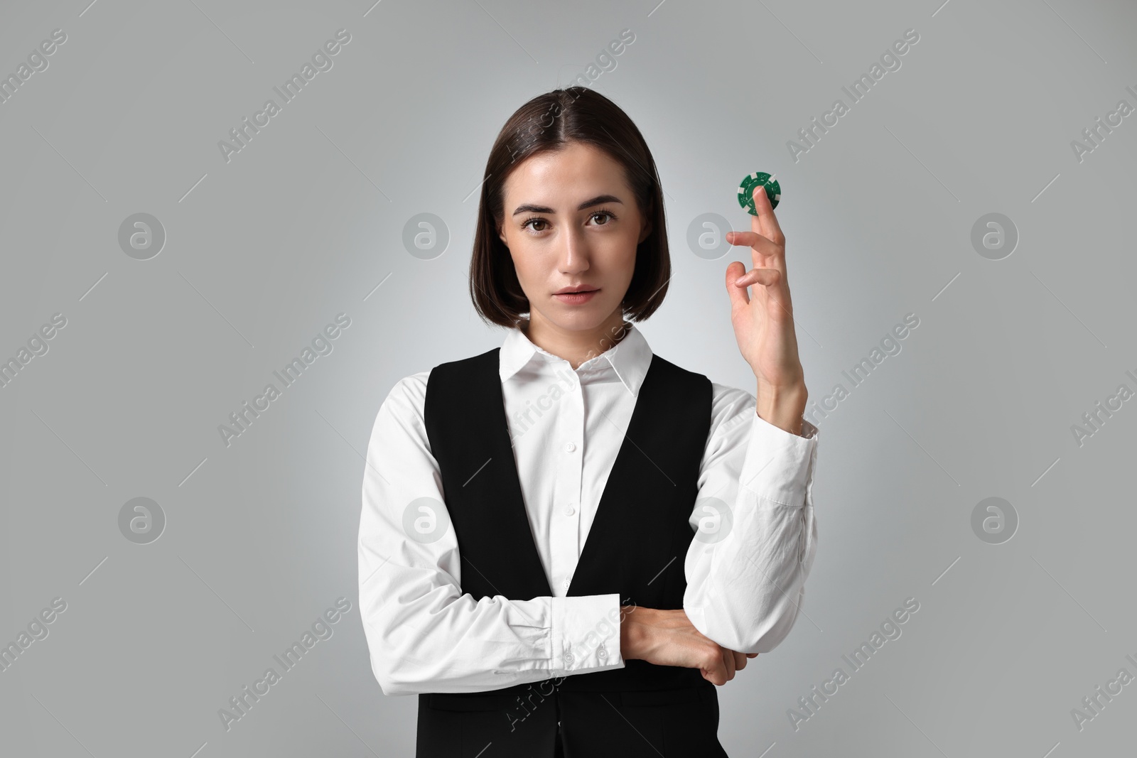 Photo of Professional croupier with casino chip on grey background