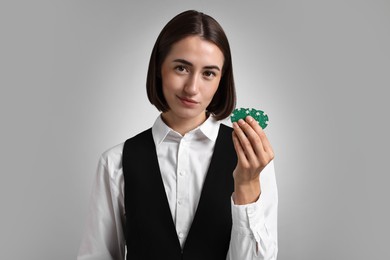 Professional croupier with casino chips on grey background