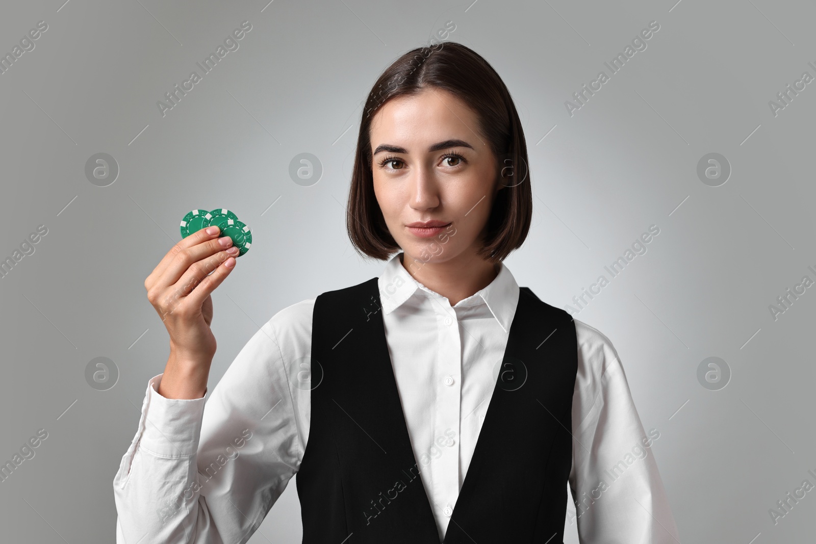 Photo of Professional croupier with casino chips on grey background