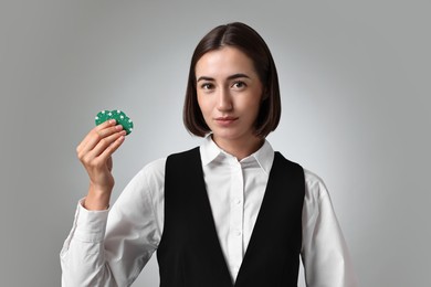 Photo of Professional croupier with casino chips on grey background