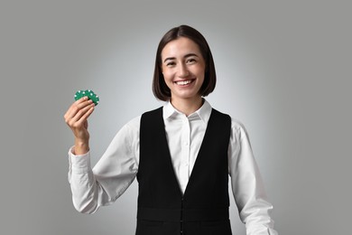 Professional croupier with casino chips on grey background