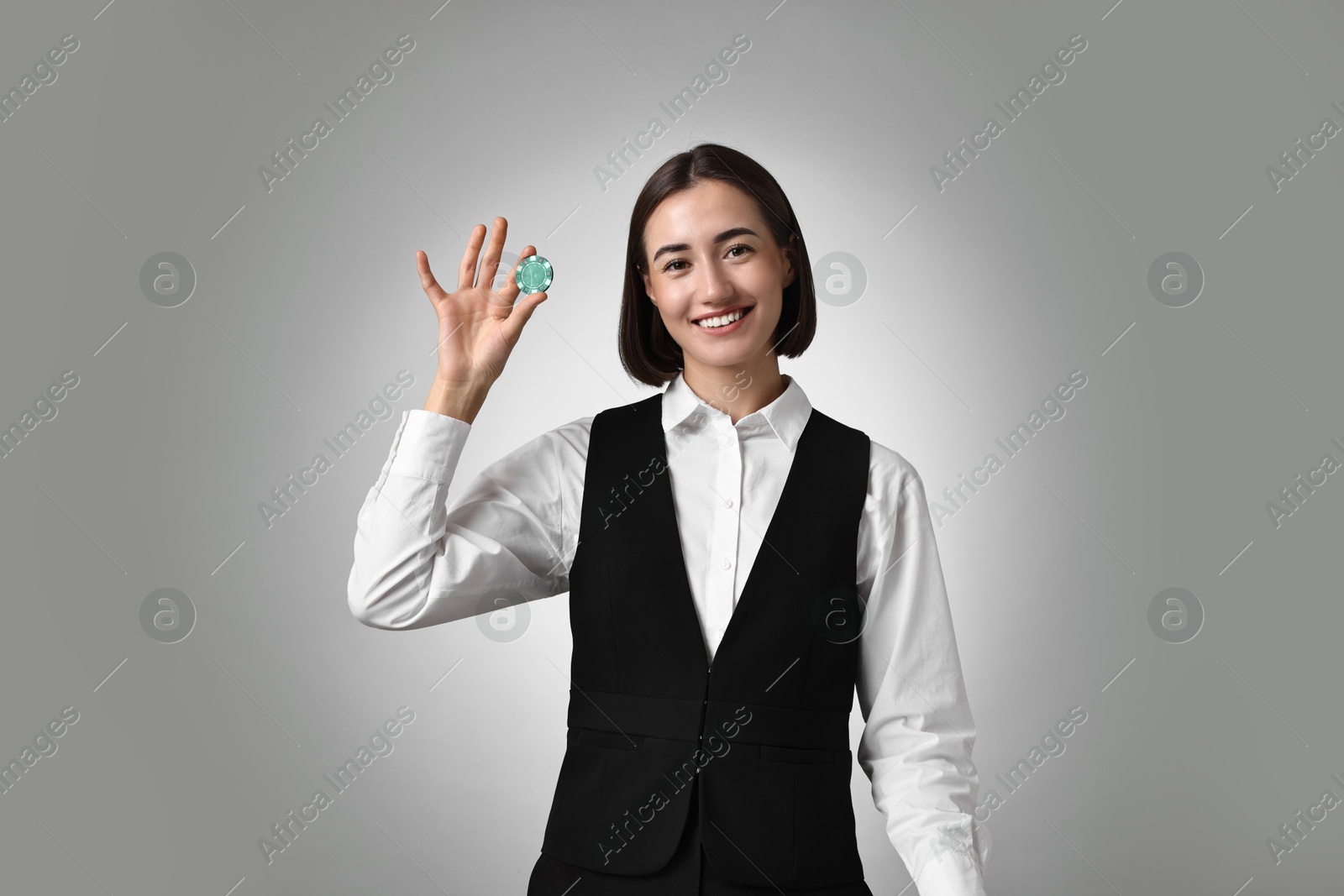 Photo of Professional croupier with casino chip on grey background