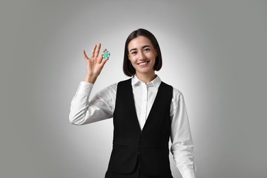 Professional croupier with casino chip on grey background