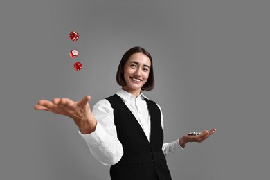 Professional croupier with dice and casino chips on grey background