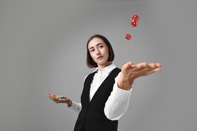 Photo of Professional croupier with dice and casino chips on grey background